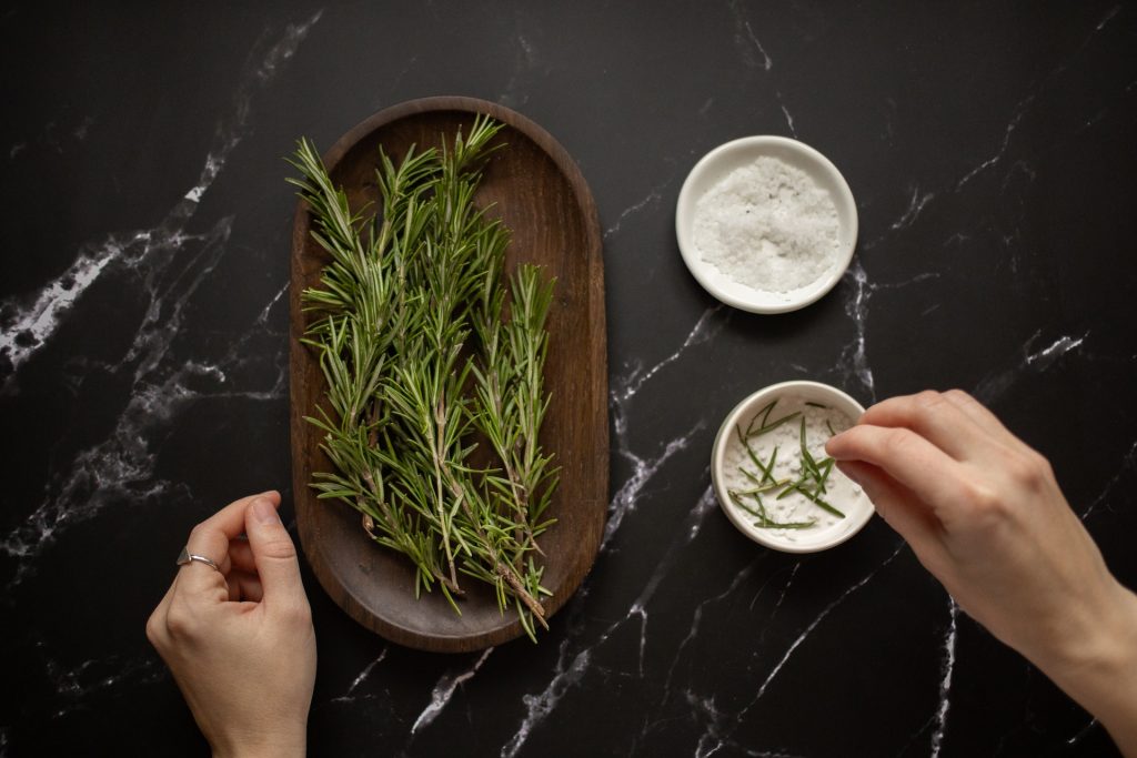 rosemary salt ingredients on a dark surface with hands mixing