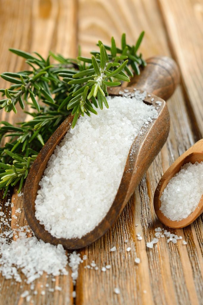 sea salt in a wooden scoop with fresh rosemary on a cutting board