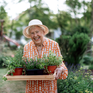 elderly woman holding tray of fresh herbs in pots