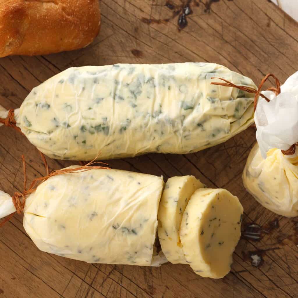compound herb butter with dried herbs wrapped in wax paper on cutting board